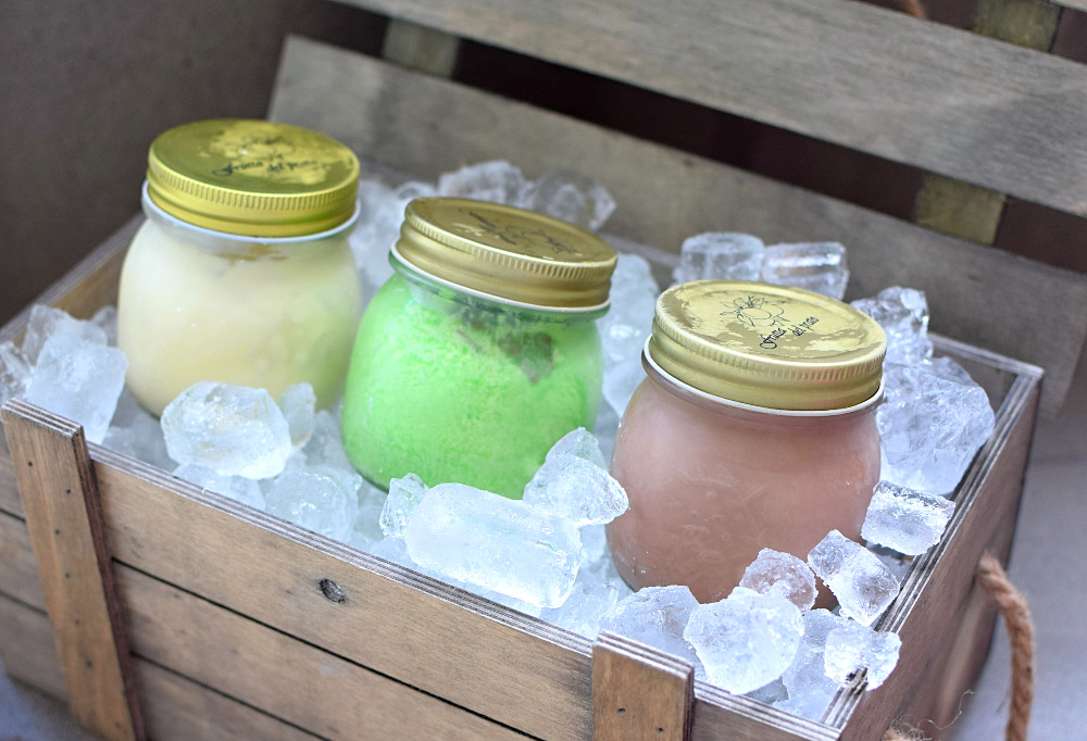 Three jars of ice cream in a wooden crate filled with ice.