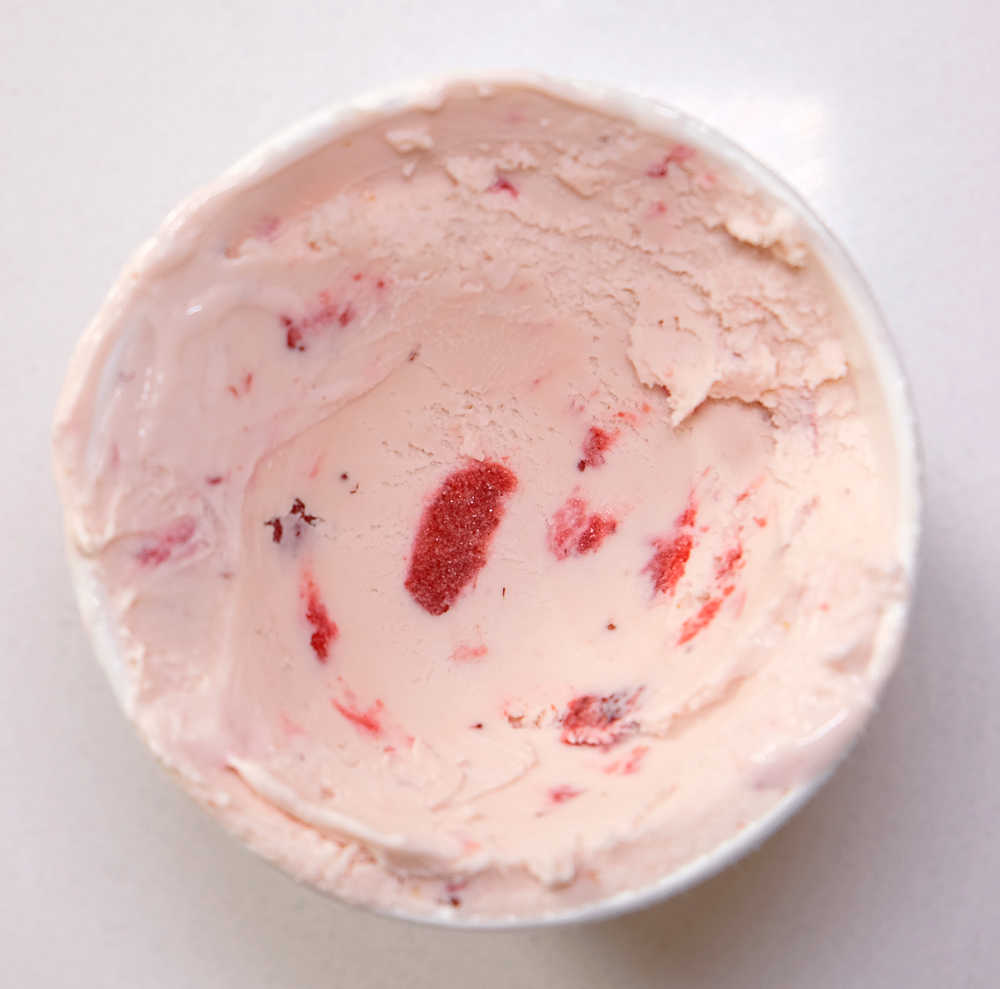 Bird's eye view of a tub of partly eaten strawberries and cream ice cream.