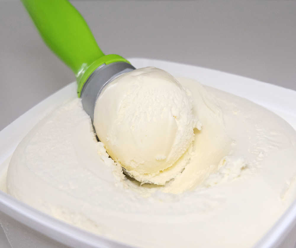 A scoop of Coles Vanilla Ice Cream resting on the top of the container.