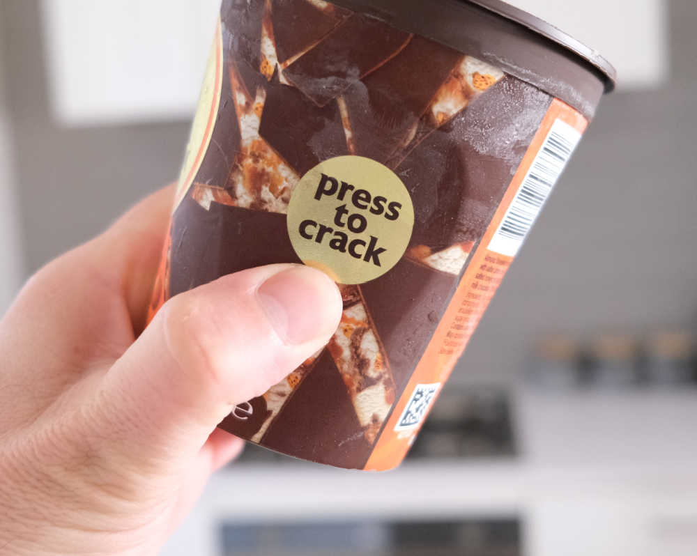 A thumb pushing on the "press to crack" button on the side of the Magnum packaging.
