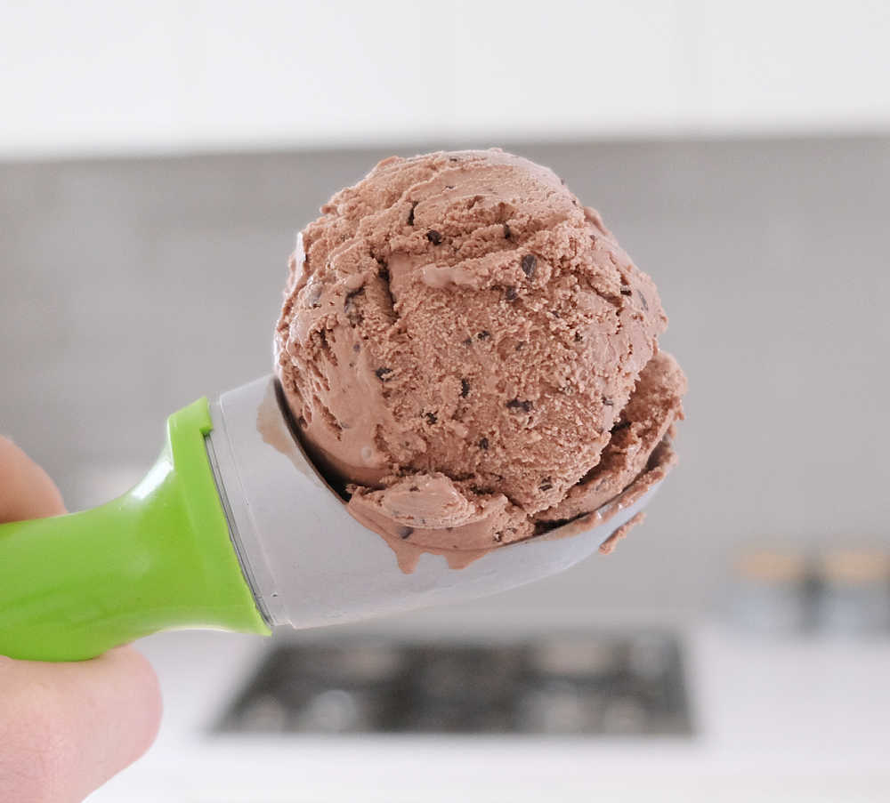 Holding a scoop of Bulla Creamy Classics Choc Chip Ice Cream with a blurred background in the background.